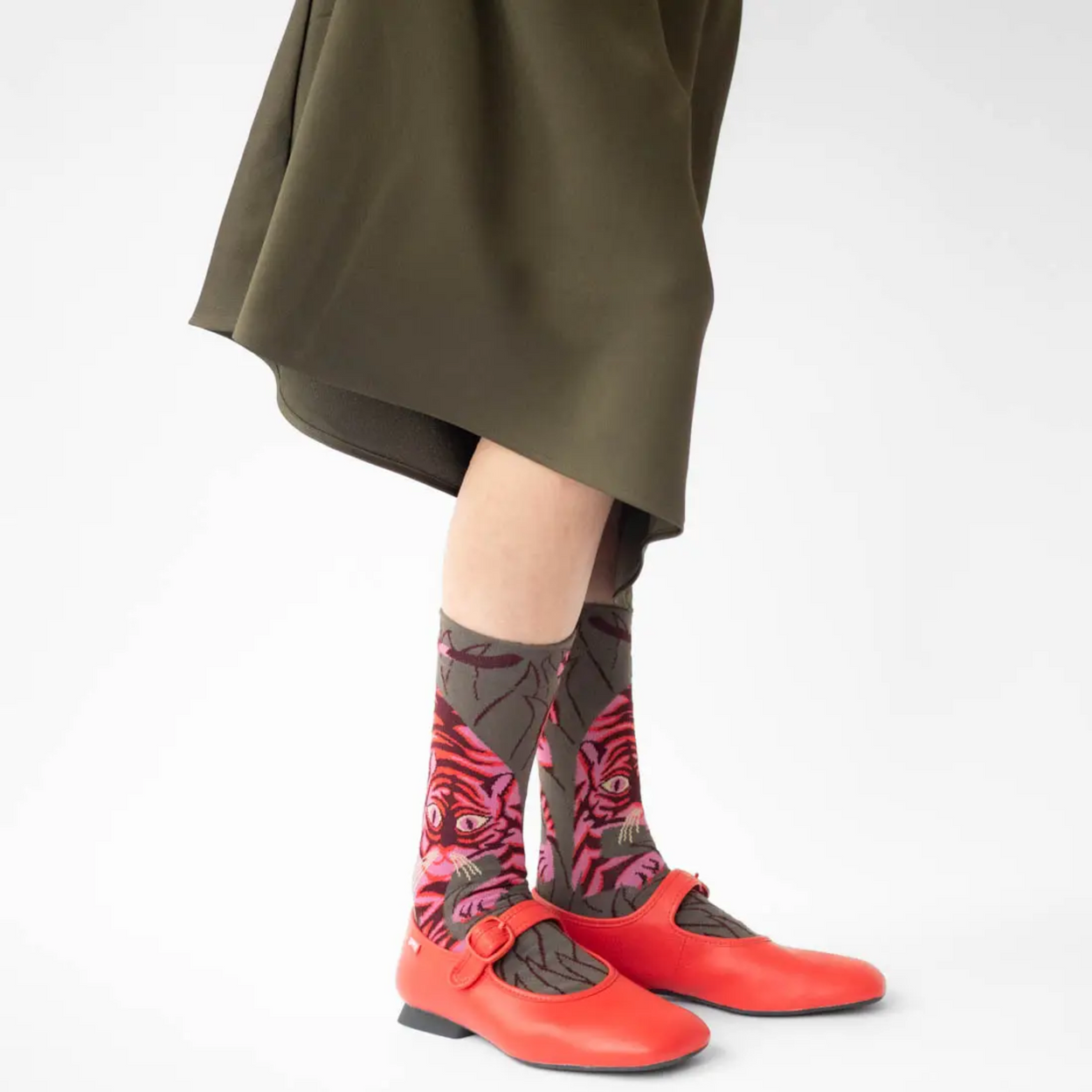 Woman with red shoes and khaki skirt wearing Bonne Maison Tiger socks against a white backdrop.