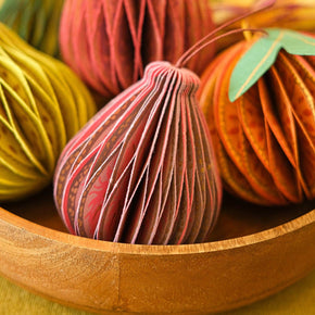 Decorative paper pumpkins in pink, green, and orange on a wooden surface with a blurred background.