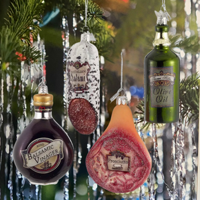 Decorative food product ornaments resembling balsamic vinegar, prosciutto, salami, and olive oil bottle on a Christmas tree.