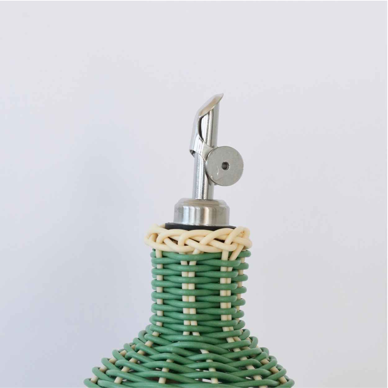 Close up of nozzle of Decorative olive oil bottle with green, brown and navy woven design and metallic nozzle on a white background