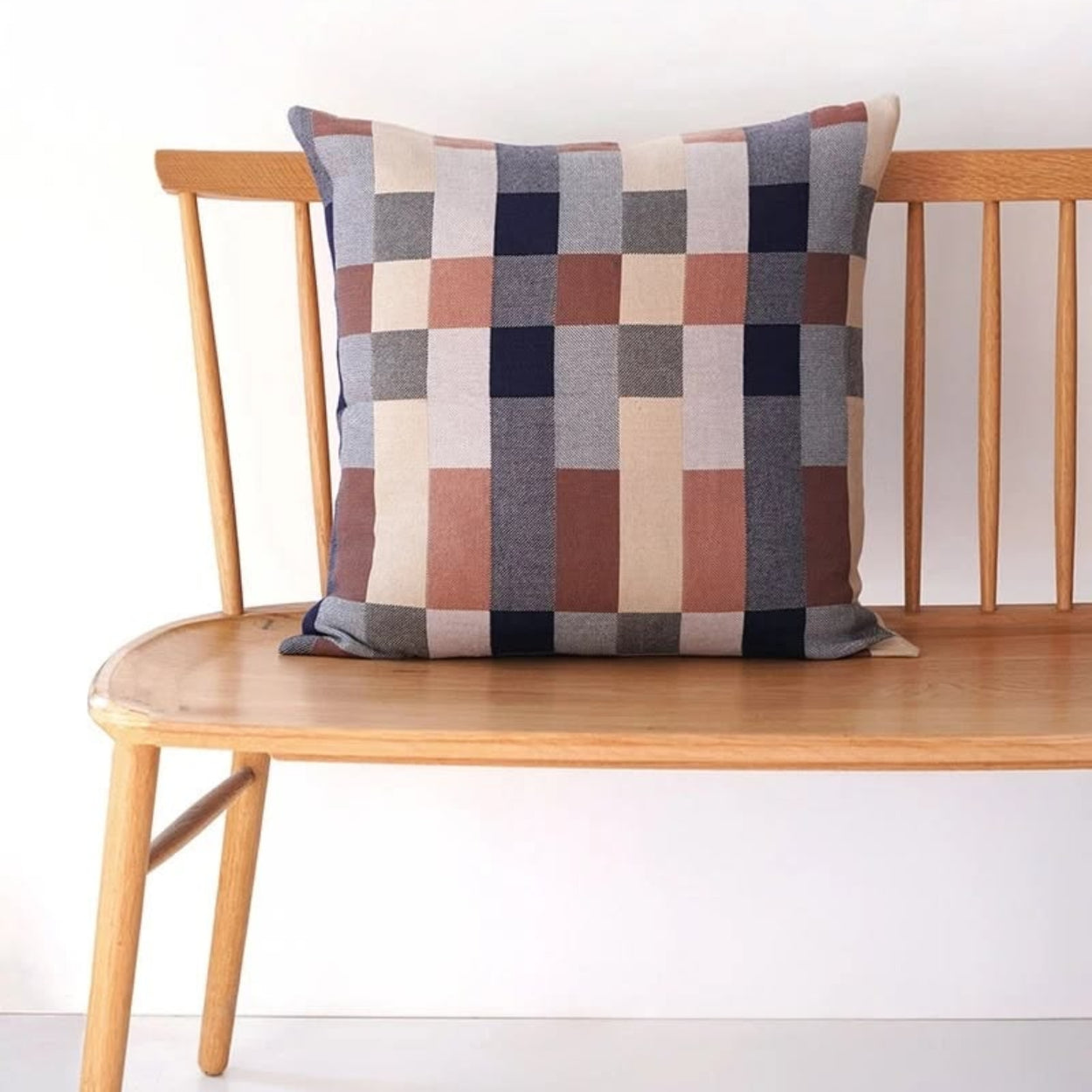 Checkered double cotton  pillow on a wooden bench against a white wall