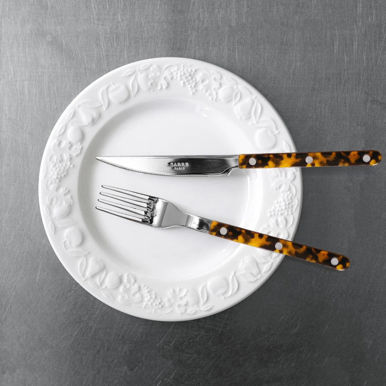 Sabre Paris Faux Tortoise knife and fork from 4 piece cutlery set, on white plate on steel benchtop.