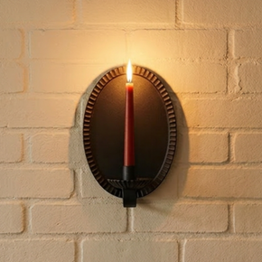Wall-mounted iron candle sconce casting a warm glow on a brick wall