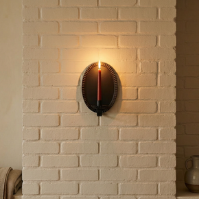 Wall-mounted candle holder with a lit candle on a brick wall