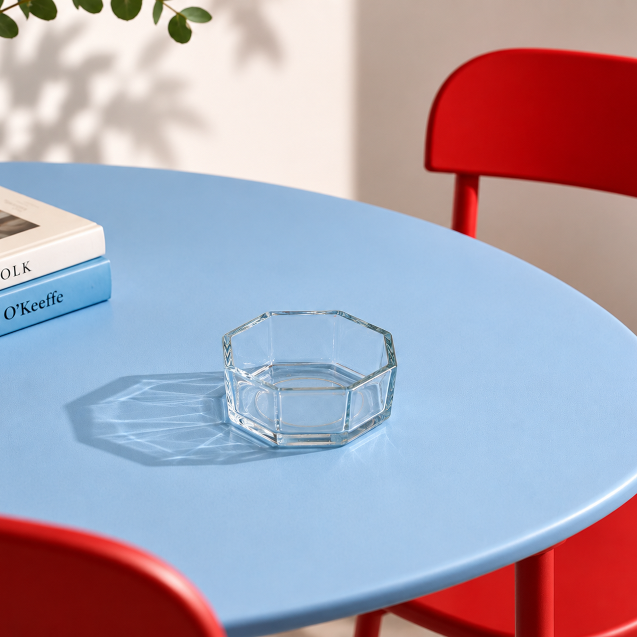Blue table with a glass bowl and books, red chair, and plant on a neutral background