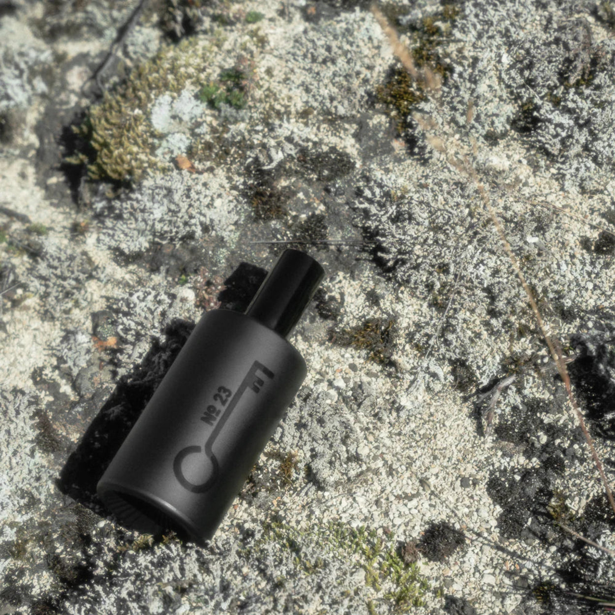 Black cylindrical EDP bottle with text on a textured stone surface