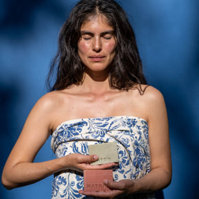 Woman in blue sarong holding two Mater Soap bars against a blue backdrop.