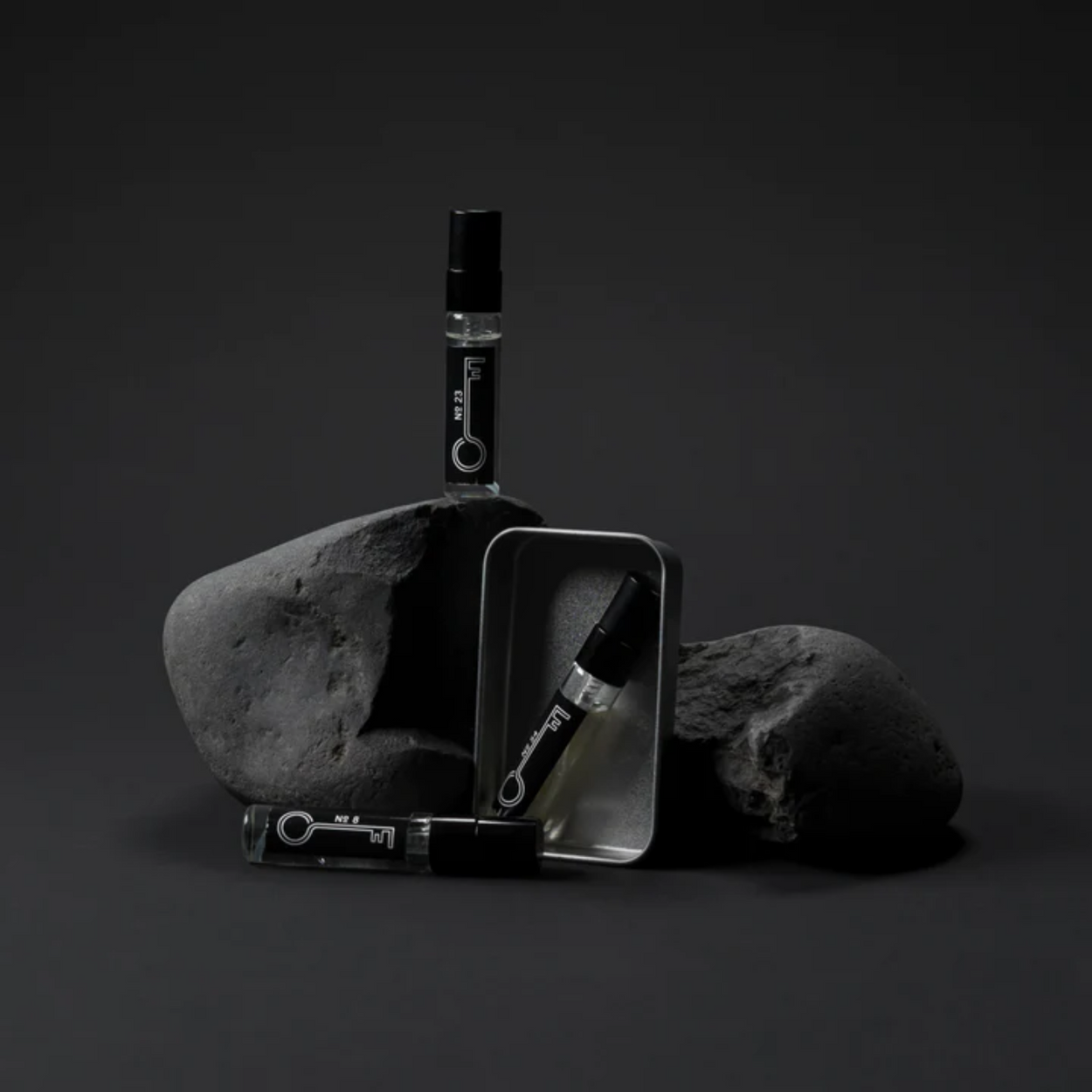 Black and white product photography of 3 small bottles of Fischersund fragrance and packaging on a dark background