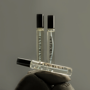 Three small perfume bottles balanced on grey stone against a grey background