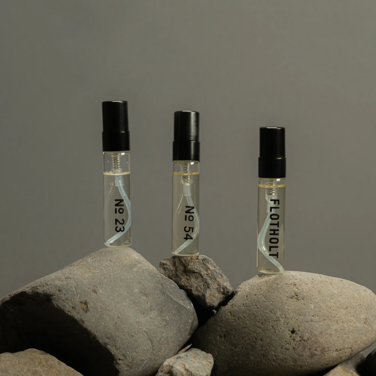 Three small perfume bottles labeled 'No 23', 'No 54', and 'FLOTHOLIT on rocks with a grey background