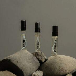 Three small perfume bottles labeled 'No 23', 'No 54', and 'FLOTHOLIT on rocks with a grey background