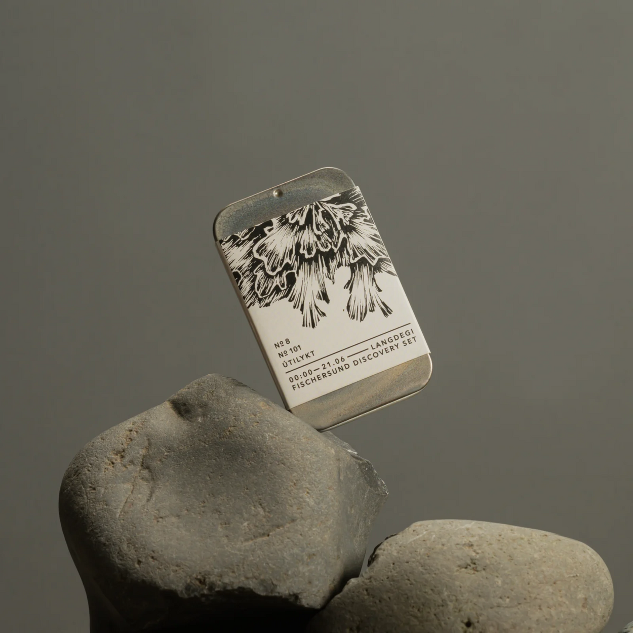 Metallic box with Fischersund Light Discovery design on a rock against a gray background