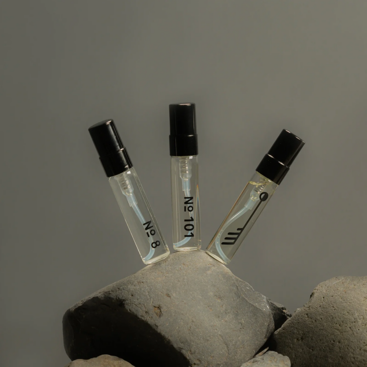 Three small perfume bottles with black caps on a stone surface against a gray background