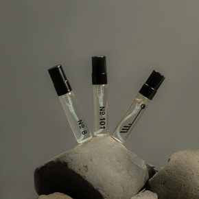Three small perfume bottles with black caps on a stone surface against a gray background