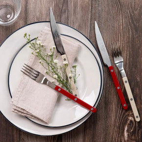 Sabre Paris Bistrot Burgundy Red and ivory Cutlery on white plate on wooden table.