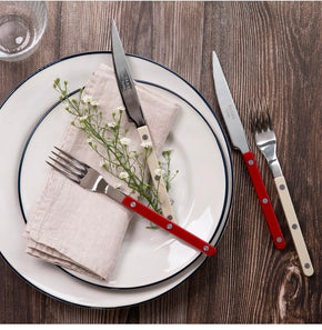 Sabre Paris Bistrot Burgundy Red and ivory Cutlery on white plate on wooden table.