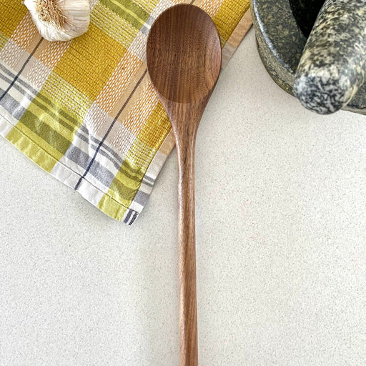 Wooden spoon on a checkered cloth with garlic and a mortar and pestle.