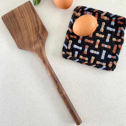 Wooden spatula and patterned trivet with eggs on a light surface