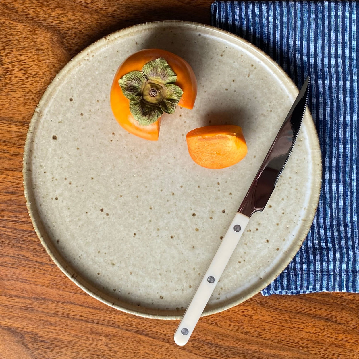 Japanese Jupiter Dinner Plate with persimmon, ivory Sabre Paris knife and napkin on wood table.