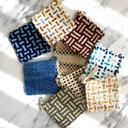 A collection of handwoven pot holders by Kate Kilmurray in various colorus displayed on a marble surface.