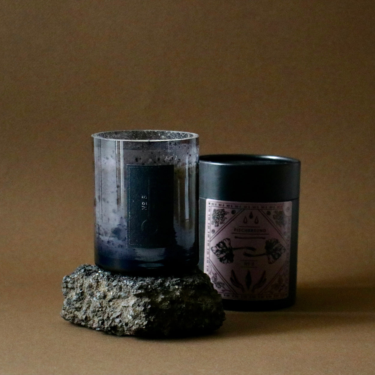 Fischersund No.8 candle on black rock with tube packaging against a brown backdrop.