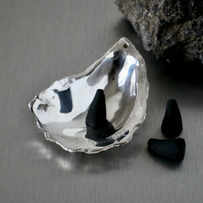 Silver oyster shell incense holders with incense cones on a stainless steel benchtop.
