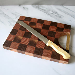 Pallares Solsona 25cm Box Wood Stainless Steel Bread Knife on marble bench with chopping board underneath..