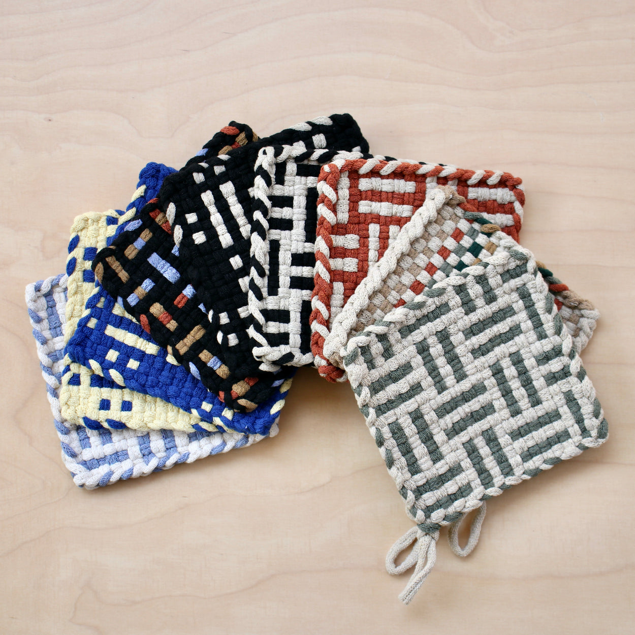 Group of Kate Kilmurray handwoven pot holders fanned out on pale wood background