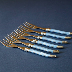 Side profile Vintage set of 6 cake forks lined up against blue backdrop.