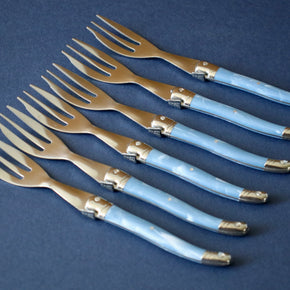 Vintage set of 6 cake forks lined up against blue backdrop.