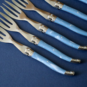 Close up of handles Vintage set of 6 cake forks lined up against blue backdrop.