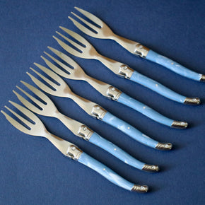 Vintage set of 6 cake forks lined up against blue backdrop.