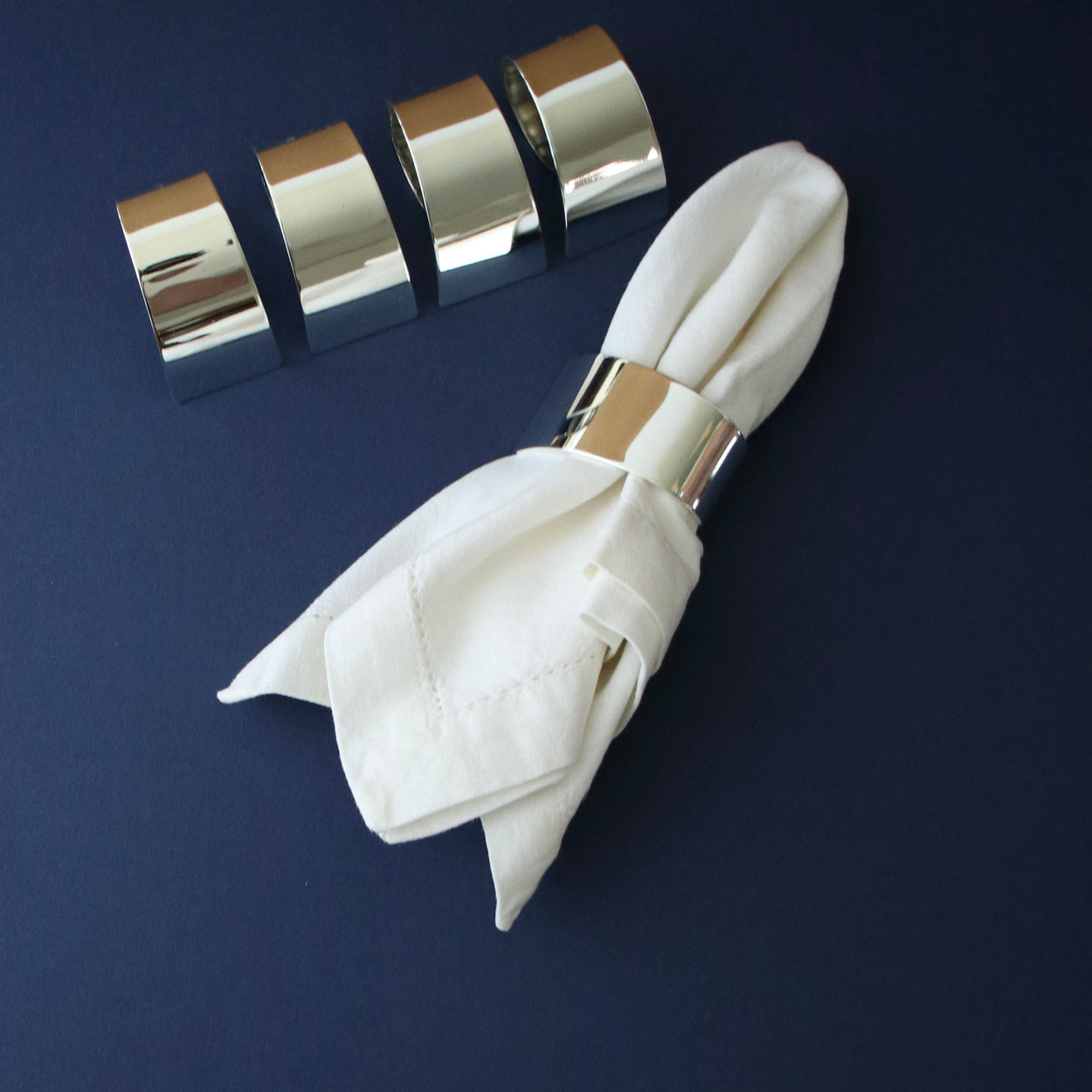 Vintage set of 4 silver plate napkin rings against dark blue backdrop, with white napkin.