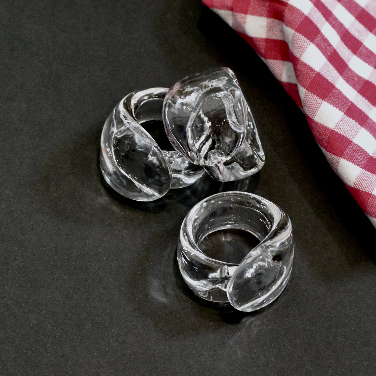 3 Vintage handmade glass napkin rings against a black background, with red gingham napkin.