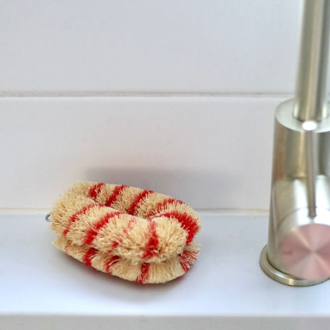 Red Japanese Striped Tawashi pot scrub brush on white tile shelf with gold tapware.