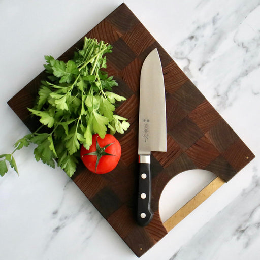 Japanese Naozumi Nihonkou 165mm Santoku Carbon Steel Kitchen Knife on chopping board with tomato, parsley and marble background.