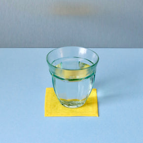 Yellow Japanese linen coaster under glass of water on a blue and grey background.