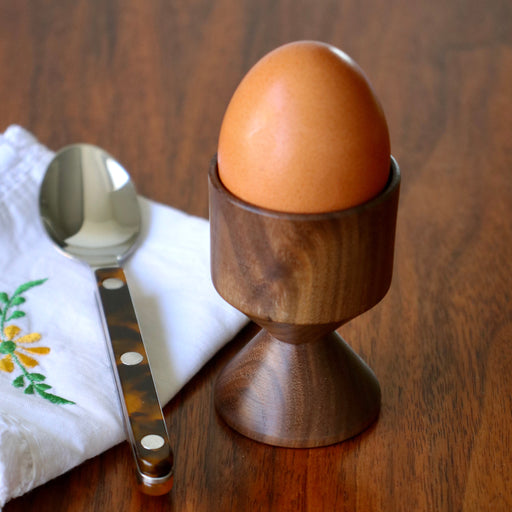 Hand crafted walnut wood egg cup with egg and Sabre Paris spoon on wood tabletop