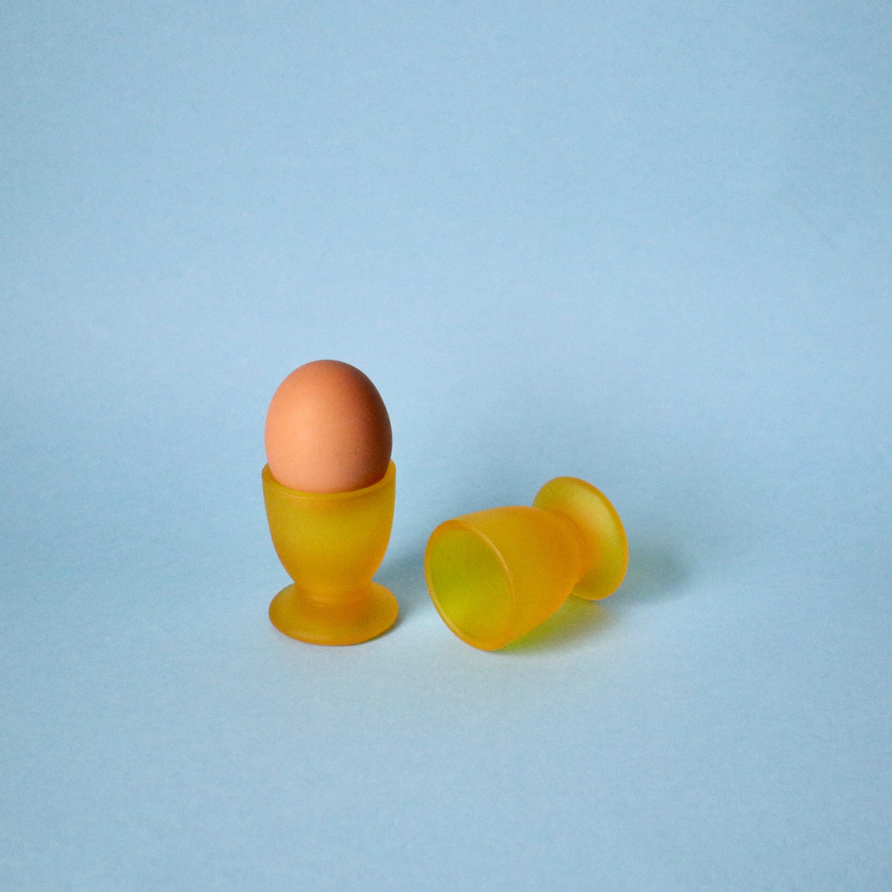 Brown egg in a yellow egg cup on a light blue background