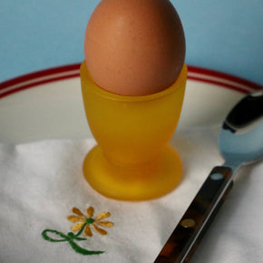 Brown egg in a yellow cup on a white plate with a floral design, next to a knife.