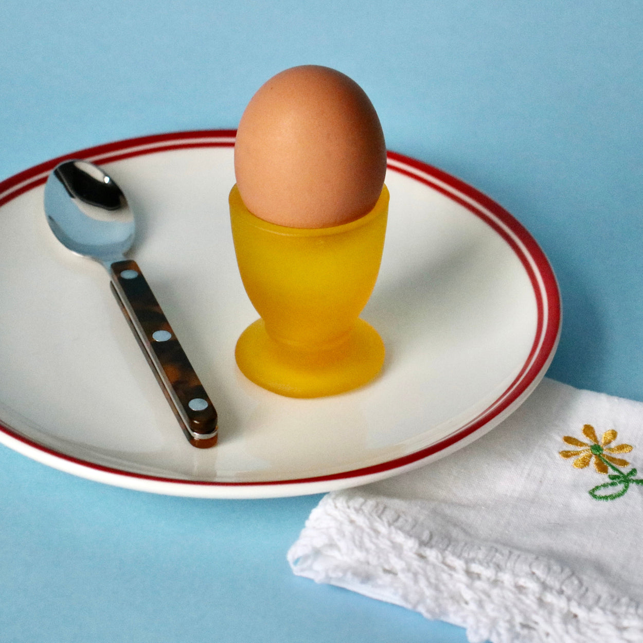 Brown egg in a yellow cup on a white plate with a blue background