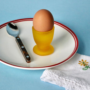 Brown egg in a yellow cup on a white plate with a blue background