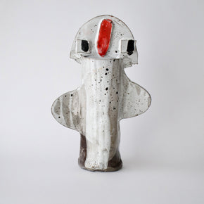 Ceramic sculpture with a white body, black speckles, and a red nose on a light grey background