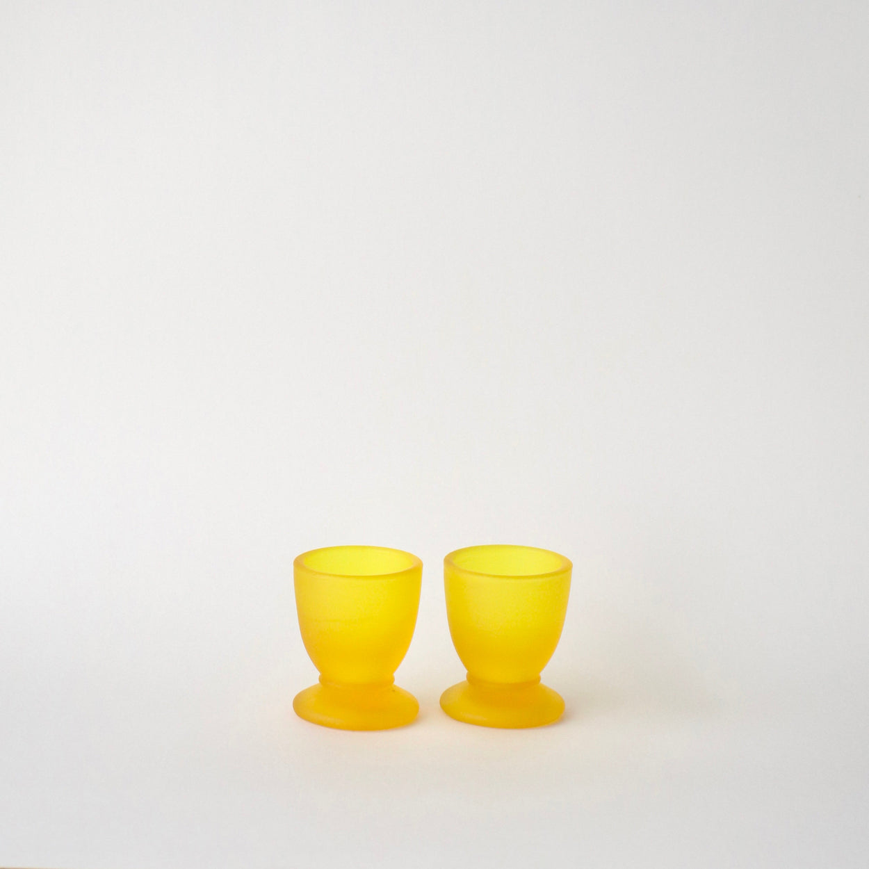 Two yellow glass egg cups on a white background