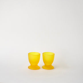 Two yellow glass egg cups on a white background