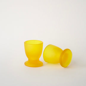 Two yellow glass egg cups on a white background