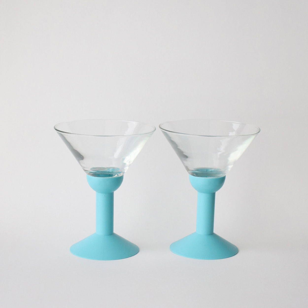 Two martini glasses with light blue bases on a white background
