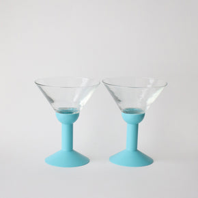 Two martini glasses with light blue bases on a white background