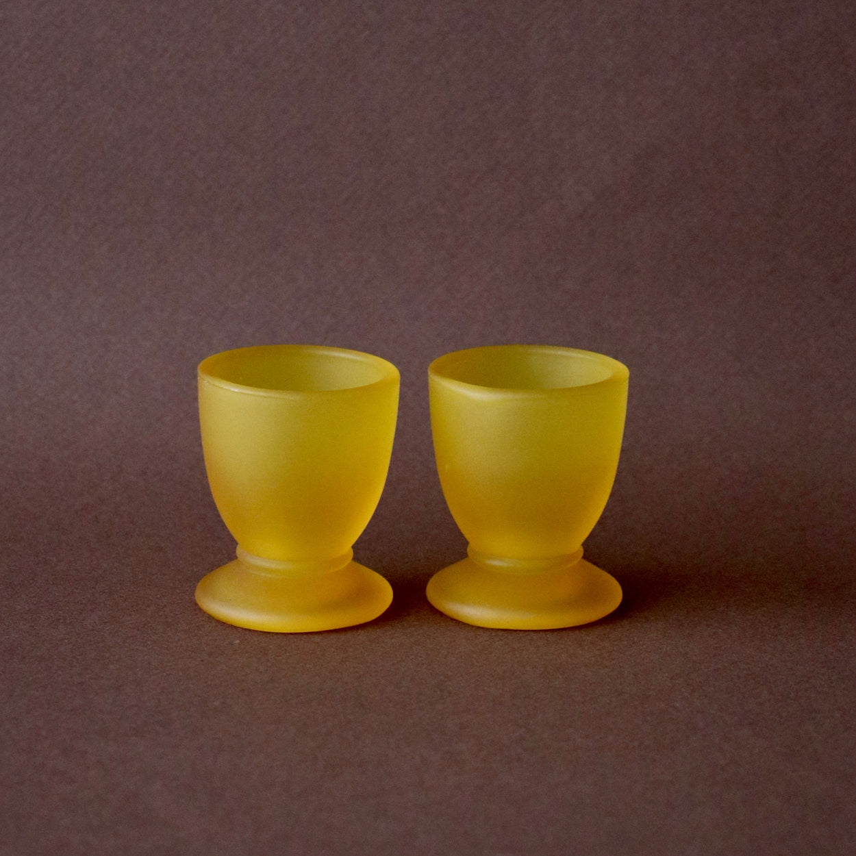 Two yellow egg cups on a brown background