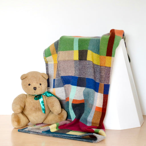 Colorful patchwork blanket draped over a white surface with a teddy bear sitting on it.